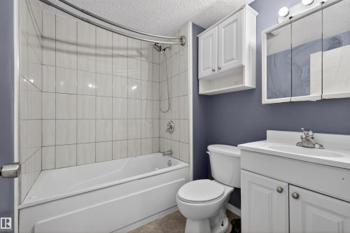 Bathroom featuring a white bathtub and shower with tiled walls, a white vanity with sink, and a mirrored medicine cabinet - 3301 139 Avenue, Edmonton, AB - Indoor Photo Showing Bathroom