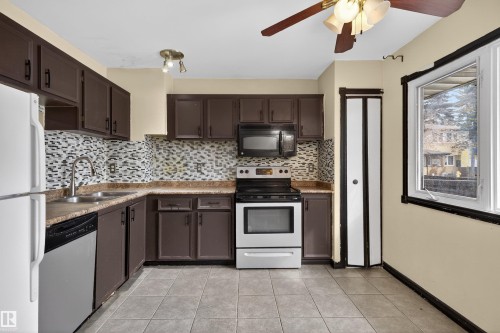 Kitchen featuring brown cabinetry, a tile backsplash, a stainless steel oven and microwave, and tile flooring - 3301 139 Avenue, Edmonton, AB - Indoor Photo Showing Kitchen With Double Sink