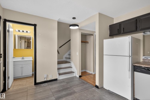 The property features a kitchen area with dark cabinetry, a white refrigerator, and a dishwasher, complemented by a stone-look countertop - 3301 139 Avenue, Edmonton, AB - Indoor Photo Showing Kitchen