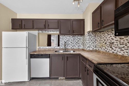 The kitchen features dark cabinetry, a mosaic tile backsplash, and a double basin stainless steel sink - 3301 139 Avenue, Edmonton, AB - Indoor Photo Showing Kitchen With Double Sink
