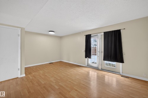 Spacious room featuring light-toned walls, wood flooring, and a glass paneled door with black drapes - 3301 139 Avenue, Edmonton, AB - Indoor Photo Showing Other Room