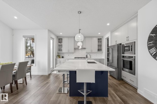 The kitchen features a center island with a white countertop and blue base, stainless steel appliances, and light-colored cabinetry - 13 Bilodeau Crescent, Beaumont, AB - Indoor Photo Showing Kitchen With Upgraded Kitchen
