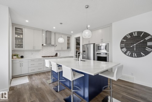 The kitchen features a large island with a white countertop and blue base, complemented by light grey cabinetry and stainless steel appliances - 13 Bilodeau Crescent, Beaumont, AB - Indoor Photo Showing Kitchen With Upgraded Kitchen