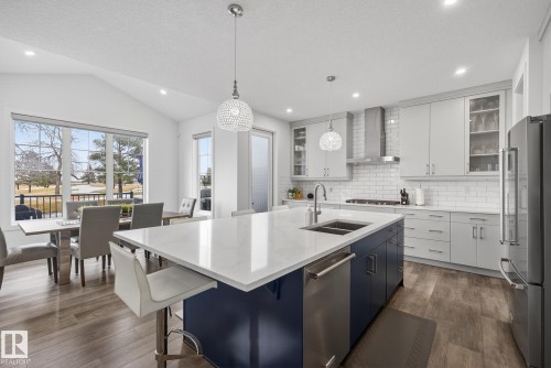 The open-concept kitchen features a large island with a double sink and seating, light-colored cabinetry, a subway tile backsplash, and stainless steel appliances - 13 Bilodeau Crescent, Beaumont, AB - Indoor Photo Showing Kitchen With Double Sink With Upgraded Kitchen