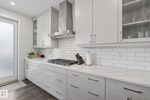 The kitchen features a gas range with a stainless steel range hood, white subway tile backsplash, and light-colored countertops - 13 Bilodeau Crescent, Beaumont, AB - Indoor Photo Showing Kitchen With Upgraded Kitchen