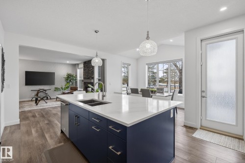 The kitchen features a spacious island with a white countertop and dark blue cabinetry, equipped with a stainless steel sink and faucet - 13 Bilodeau Crescent, Beaumont, AB - Indoor Photo Showing Kitchen With Double Sink
