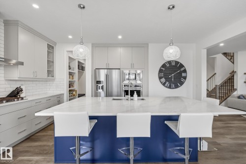 The kitchen features a spacious island with a blue base and white countertop, complemented by light grey cabinetry and stainless steel appliances - 13 Bilodeau Crescent, Beaumont, AB - Indoor Photo Showing Kitchen With Double Sink With Upgraded Kitchen