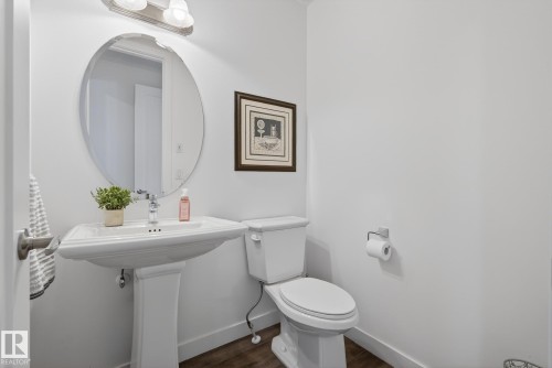 The bathroom features a pedestal sink with a chrome faucet, an oval mirror, and a toilet - 13 Bilodeau Crescent, Beaumont, AB - Indoor Photo Showing Bathroom