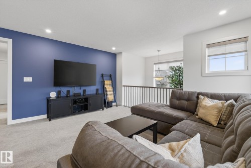 Living area featuring light grey carpeting, a prominent blue accent wall, and a window providing natural light - 13 Bilodeau Crescent, Beaumont, AB - Indoor Photo Showing Living Room