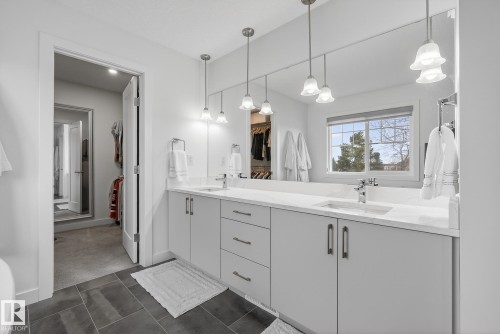 Well-appointed bathroom featuring a double vanity with light-colored cabinetry and countertop, a large mirror, and hanging light fixtures - 13 Bilodeau Crescent, Beaumont, AB - Indoor Photo Showing Bathroom