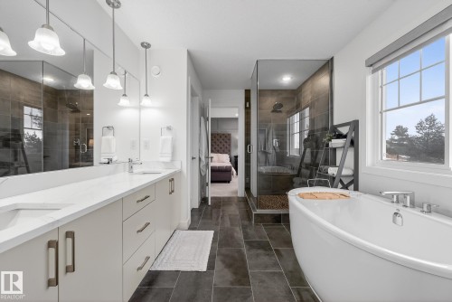 This bathroom features a double vanity with ample counter space, a spacious walk-in shower with a glass enclosure, and a freestanding soaking tub - 13 Bilodeau Crescent, Beaumont, AB - Indoor Photo Showing Bathroom