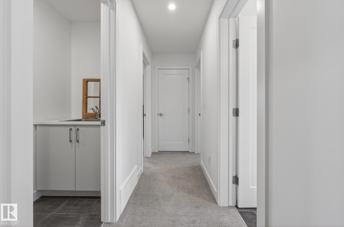 Well-lit hallway with carpeted flooring and white doors leading to various areas - 13 Bilodeau Crescent, Beaumont, AB - Indoor Photo Showing Other Room