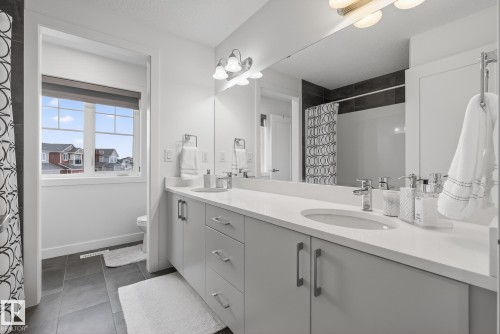 The bathroom features a double vanity with light gray cabinetry, white countertops, and modern light fixtures - 13 Bilodeau Crescent, Beaumont, AB - Indoor Photo Showing Bathroom