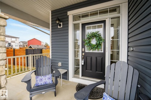The property features a welcoming front porch with a stone pillar, dark gray siding, and a dark front door with glass panels - 13 Bilodeau Crescent, Beaumont, AB - Outdoor With Exterior