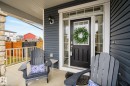 The property features a welcoming front porch with a stone pillar, dark gray siding, and a dark front door with glass panels - 13 Bilodeau Crescent, Beaumont, AB  - Outdoor With Exterior 