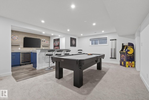 The property features a finished entertainment area with carpeted flooring, a dedicated bar area with blue cabinetry, and a recessed window - 13 Bilodeau Crescent, Beaumont, AB - Indoor Photo Showing Other Room