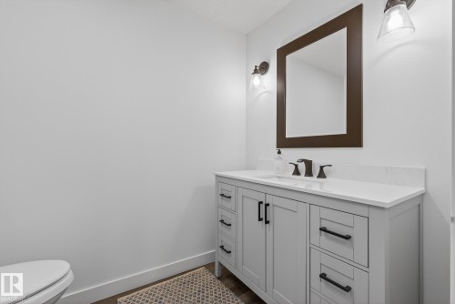 Bathroom featuring a vanity with a white countertop, dark-toned hardware, and a framed mirror with sconce lighting - 13 Bilodeau Crescent, Beaumont, AB - Indoor Photo Showing Bathroom