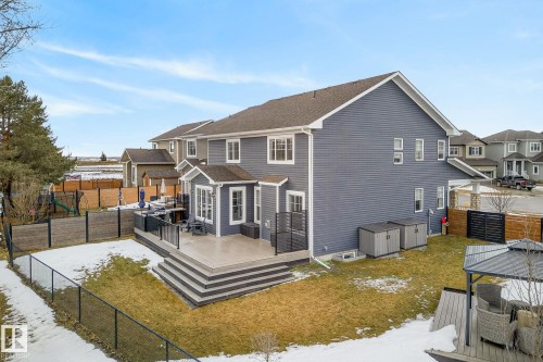 The property features an extensive rear deck with dark railings and steps, an expansive lawn, and two outdoor storage sheds - 13 Bilodeau Crescent, Beaumont, AB - Outdoor With Deck Patio Veranda With Exterior