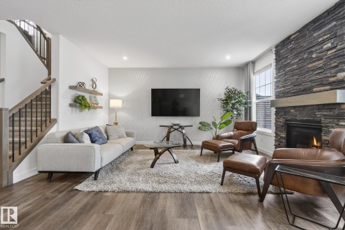 The living room features wood-style flooring, a stone-accented fireplace, and a staircase with wooden handrails and black balusters - 13 Bilodeau Crescent, Beaumont, AB - Indoor Photo Showing Living Room With Fireplace