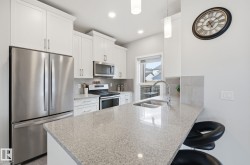 The kitchen features a stainless steel refrigerator and microwave, white cabinetry, a light-colored countertop, and a double basin sink with a chrome faucet - 