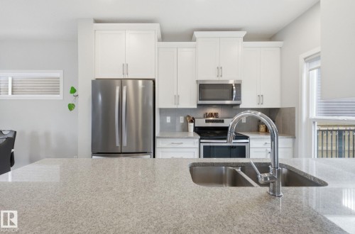 The kitchen features a double basin sink with a high-arc faucet, light-colored countertops, white cabinetry, and stainless steel appliances - 17498 76 St Nw, Edmonton, AB - Indoor Photo Showing Kitchen With Double Sink With Upgraded Kitchen