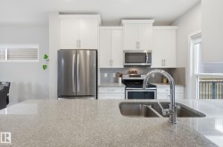 The kitchen features a double basin sink with a high-arc faucet, light-colored countertops, white cabinetry, and stainless steel appliances - 