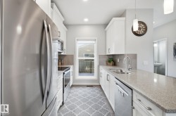 The kitchen features stainless steel appliances, a double basin sink, light-colored countertops, and white cabinetry - 