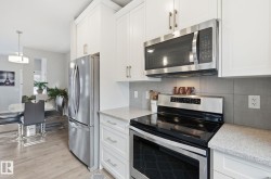 The kitchen features white cabinetry, stainless steel appliances, and light-colored countertops - 