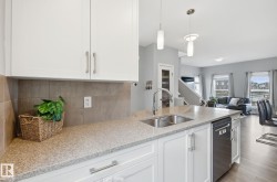 The kitchen features white cabinetry, a double basin sink with a chrome faucet, and integrated stainless steel dishwasher - 