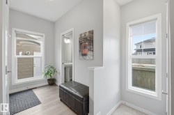 Entryway featuring light-toned flooring, two windows, and a doorway leading to a powder room with a pedestal sink - 