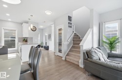 The open concept main living area features hardwood floors, a kitchen island with seating, and a staircase with carpeted treads - 
