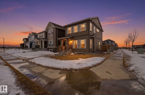 The property features a two-story exterior with siding and stone accents, a covered front porch, and illuminated windows - 17498 76 St Nw, Edmonton, AB - Outdoor