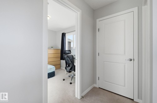 The property features light gray walls and carpeted flooring throughout the hallway and into the adjacent room, which includes a window with dark curtains - 17498 76 St Nw, Edmonton, AB - Indoor Photo Showing Other Room