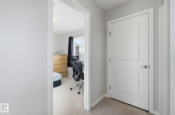 The property features light gray walls and carpeted flooring throughout the hallway and into the adjacent room, which includes a window with dark curtains - 
