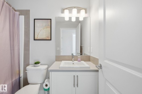This bathroom features a white vanity with a rectangular sink, a mirror, and a wall-mounted light fixture - 17498 76 St Nw, Edmonton, AB - Indoor Photo Showing Bathroom