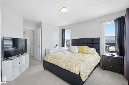 This room features light-colored walls, carpeted flooring, and two windows with dark curtains - 17498 76 St Nw, Edmonton, AB - Indoor Photo Showing Bedroom