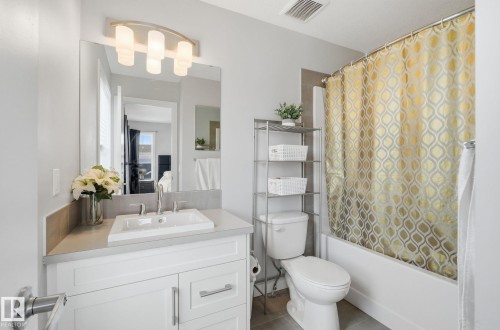 The bathroom features a vanity with a rectangular sink, a mirror with an overhead light fixture, and a bathtub with a shower curtain - 17498 76 St Nw, Edmonton, AB - Indoor Photo Showing Bathroom