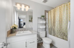 The bathroom features a vanity with a rectangular sink, a mirror with an overhead light fixture, and a bathtub with a shower curtain - 