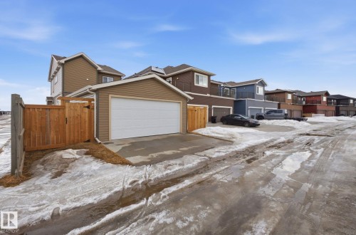 The property features a detached garage with a white overhead door and tan siding, a wood fence, and a paved driveway - 17498 76 St Nw, Edmonton, AB - Outdoor