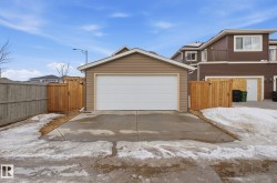 The property includes a detached garage with a white garage door, featuring light brown siding and a brown shingled roof - 