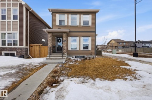 The property features a two-story exterior with brown siding and white window shutters, complemented by a front porch with stone accents and a concrete walkway - 17498 76 St Nw, Edmonton, AB - Outdoor With Facade