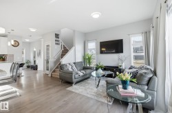 Spacious open concept living area featuring light-toned flooring, large windows, and a staircase - 
