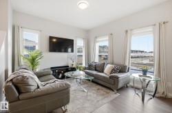 Living area with hardwood flooring, light-colored walls, and large windows with drapes - 