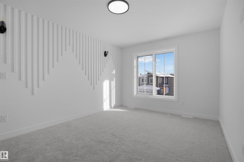This room features a decorative accent wall with vertical white panels, a large window providing natural light, and plush grey carpeting - 3304 Chickadee Drive, Edmonton, AB - Indoor Photo Showing Other Room