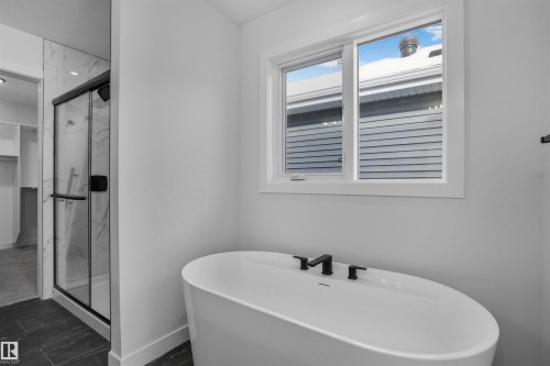 Bathroom featuring a freestanding oval tub with matte black fixtures, a window providing natural light, and a shower with a clear glass enclosure and marble-patterned walls - 3304 Chickadee Drive, Edmonton, AB - Indoor Photo Showing Bathroom