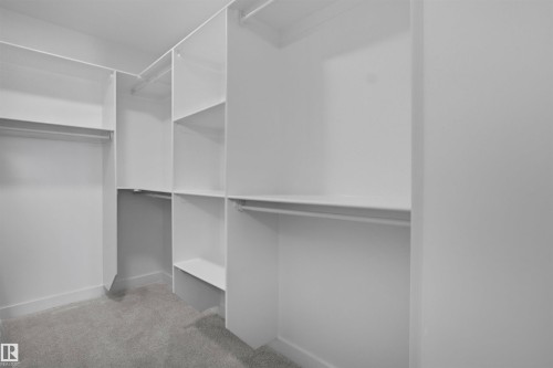 This walk-in closet features white built-in shelving, hanging rods, and light gray carpeting - 3304 Chickadee Drive, Edmonton, AB - Indoor With Storage