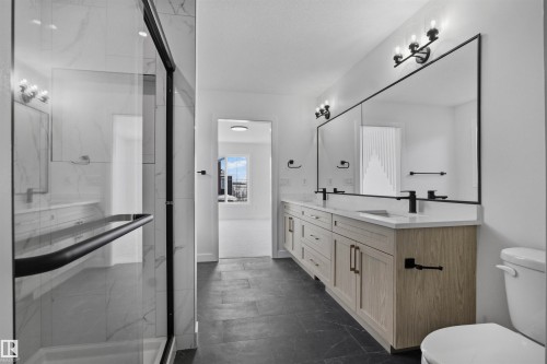 Well-appointed bathroom featuring a spacious walk-in shower with glass enclosure, a dual vanity with light-toned cabinetry and white countertops, and a large mirror with contemporary lighting fixtures - 3304 Chickadee Drive, Edmonton, AB - Indoor Photo Showing Bathroom