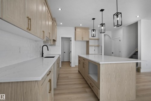 The kitchen features light-toned cabinetry with brass hardware, a white subway tile backsplash, and a spacious island with a white countertop - 3304 Chickadee Drive, Edmonton, AB - Indoor Photo Showing Kitchen With Upgraded Kitchen