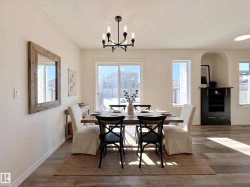 This dining area features light-colored walls, a sliding glass door, and a modern chandelier - 17127 7A Avenue, Edmonton, AB - Indoor Photo Showing Dining Room