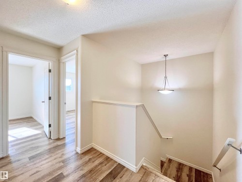 Hallway and stairwell featuring hardwood style flooring, a neutral color palette, and a hanging light fixture - 17127 7A Avenue, Edmonton, AB - Indoor Photo Showing Other Room
